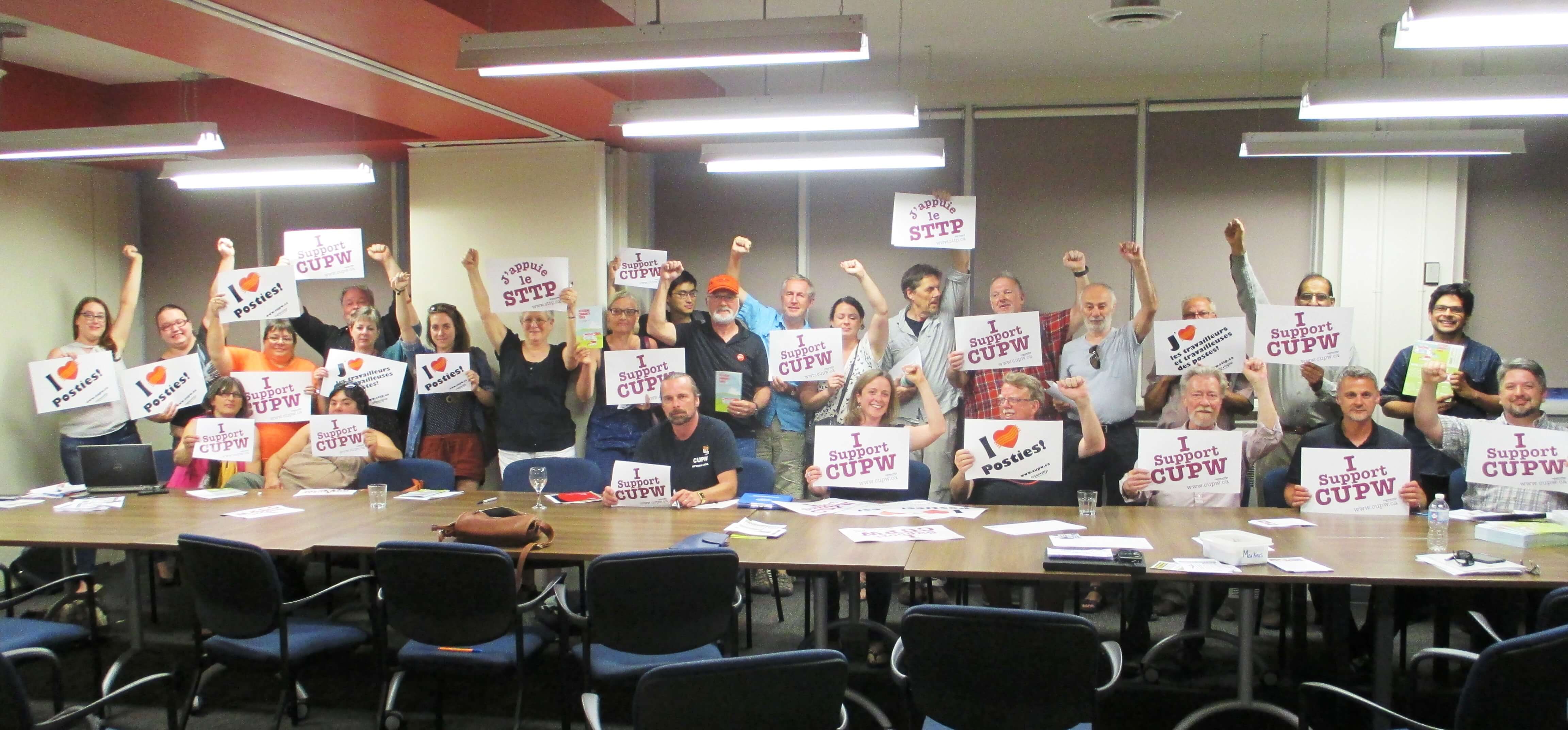 Groupe de personnes du collectif « Solidarité contre l’austérité » tenant des pancartes en appui aux travailleurs et travailleuses des postes.